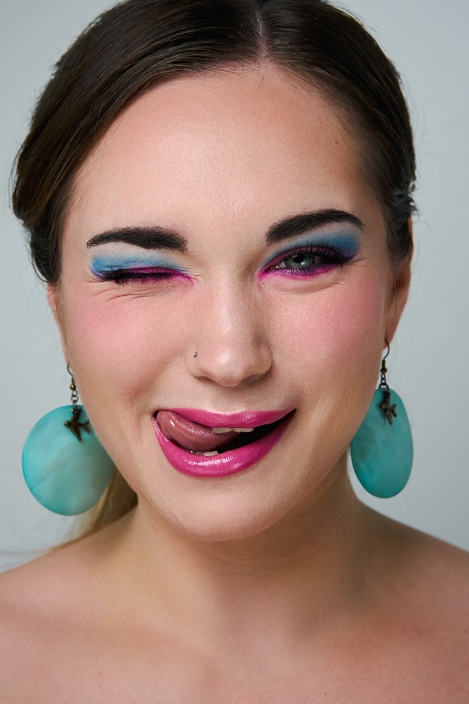 Model mit pink-blauem Augen-Makeup streckt Zunge raus 