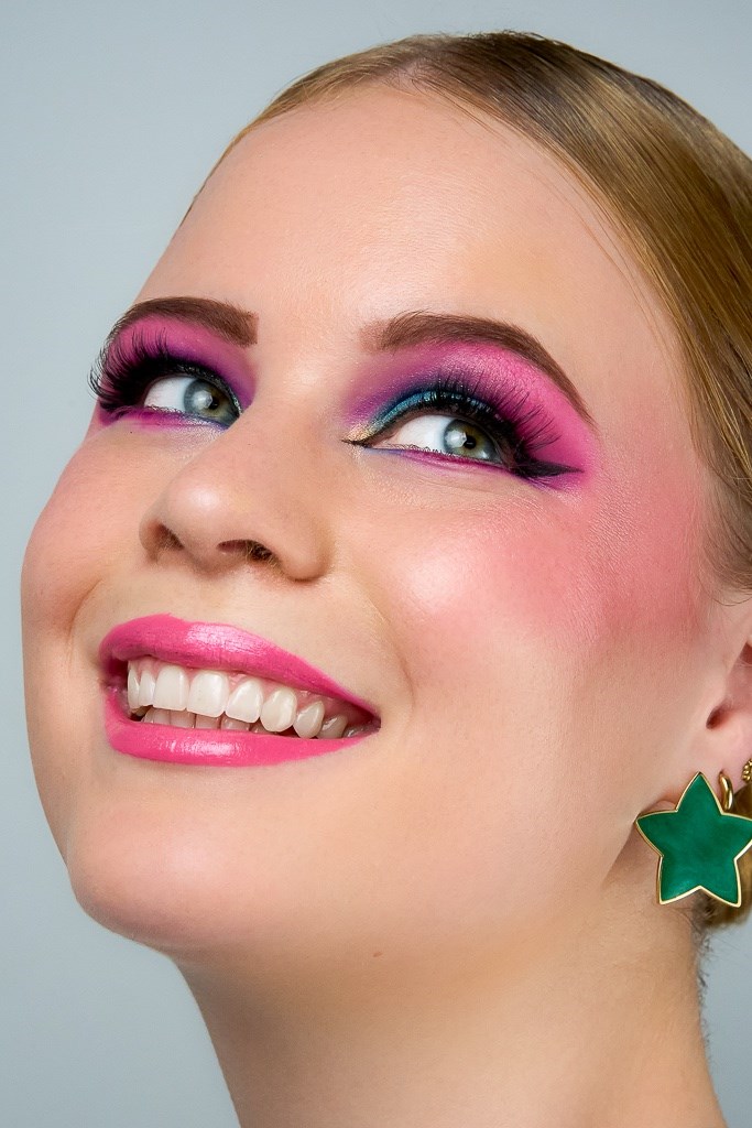Model mit buntem Lidschatten und pinkem Lippenstift lacht und schaut schräg nach oben